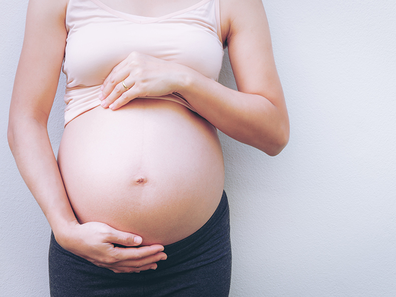 A photograph of a pregnant woman's exposed stomach, with her hands lovingly supporting her stomach